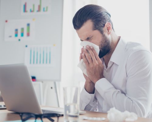 Sick businessman with temperature works in office and wipes his nose with a napkin